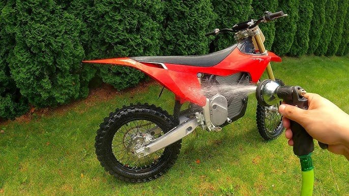 Electric dirt bike being safely washed with a low-pressure hose after trail riding